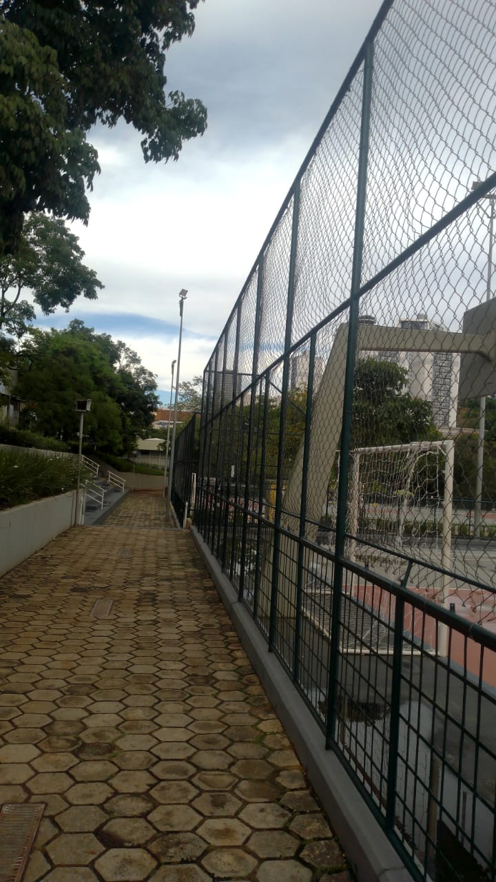 Quadra esportiva cercada com calçada de piso intertravado